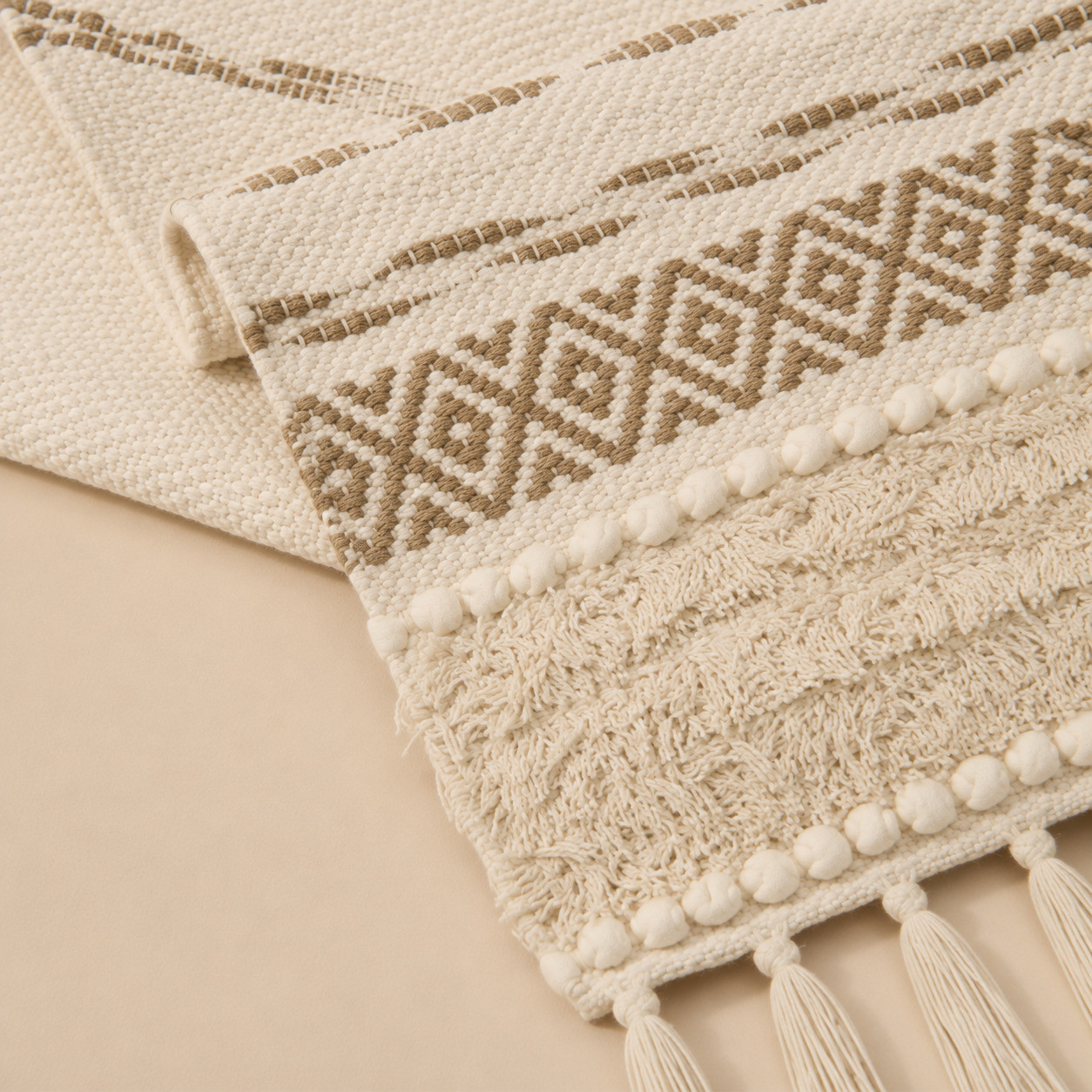 Boho table runner with geometric diamond weave and pom-pom trim detail close-up