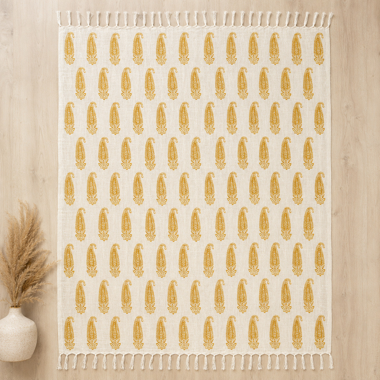 Flat lay of ivory cotton throw with mustard paisley handblock print and tasseled edges