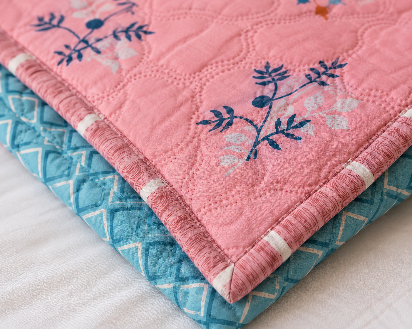 Close-up corner of pink quilted comforter showing floral print and teal geometric reverse with striped piping