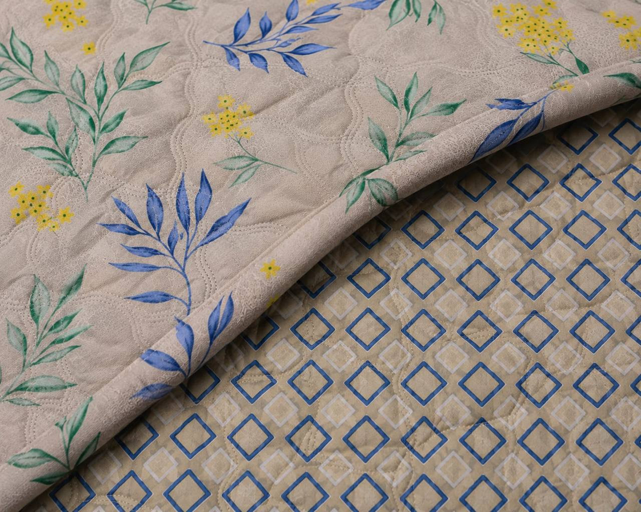 Close-up of beige cotton quilted comforter with blue-green leaf print showing reversible blue diamond lattice lining