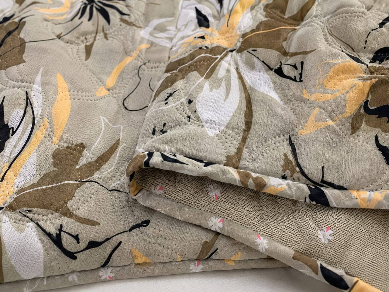 Close-up of beige floral print cotton quilted comforter showing wave-stitch quilting and reversible ditsy floral lining