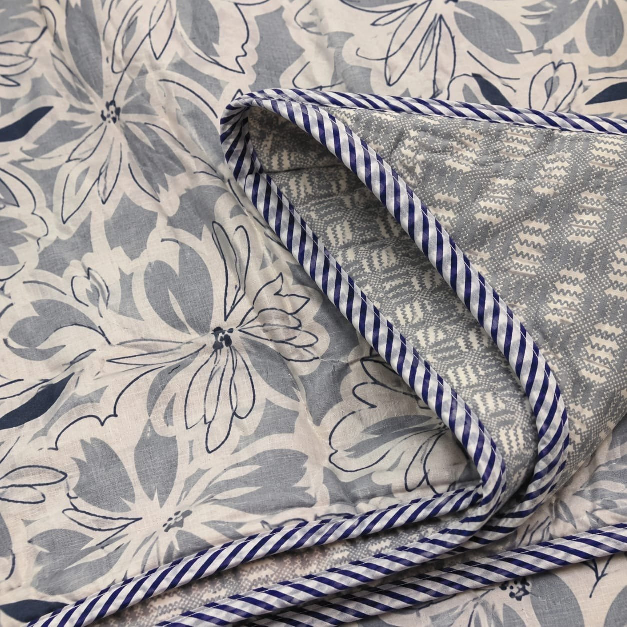 Close-up of folded cotton dohar corner showing floral print chevron reverse and corded edge piping