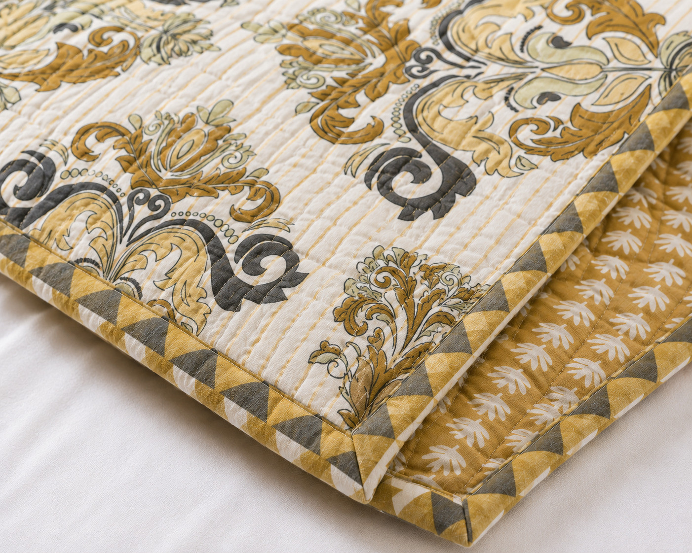 Close-up of folded golden damask quilted comforter showing scroll print and reverse leaf sprig pattern with diamond border