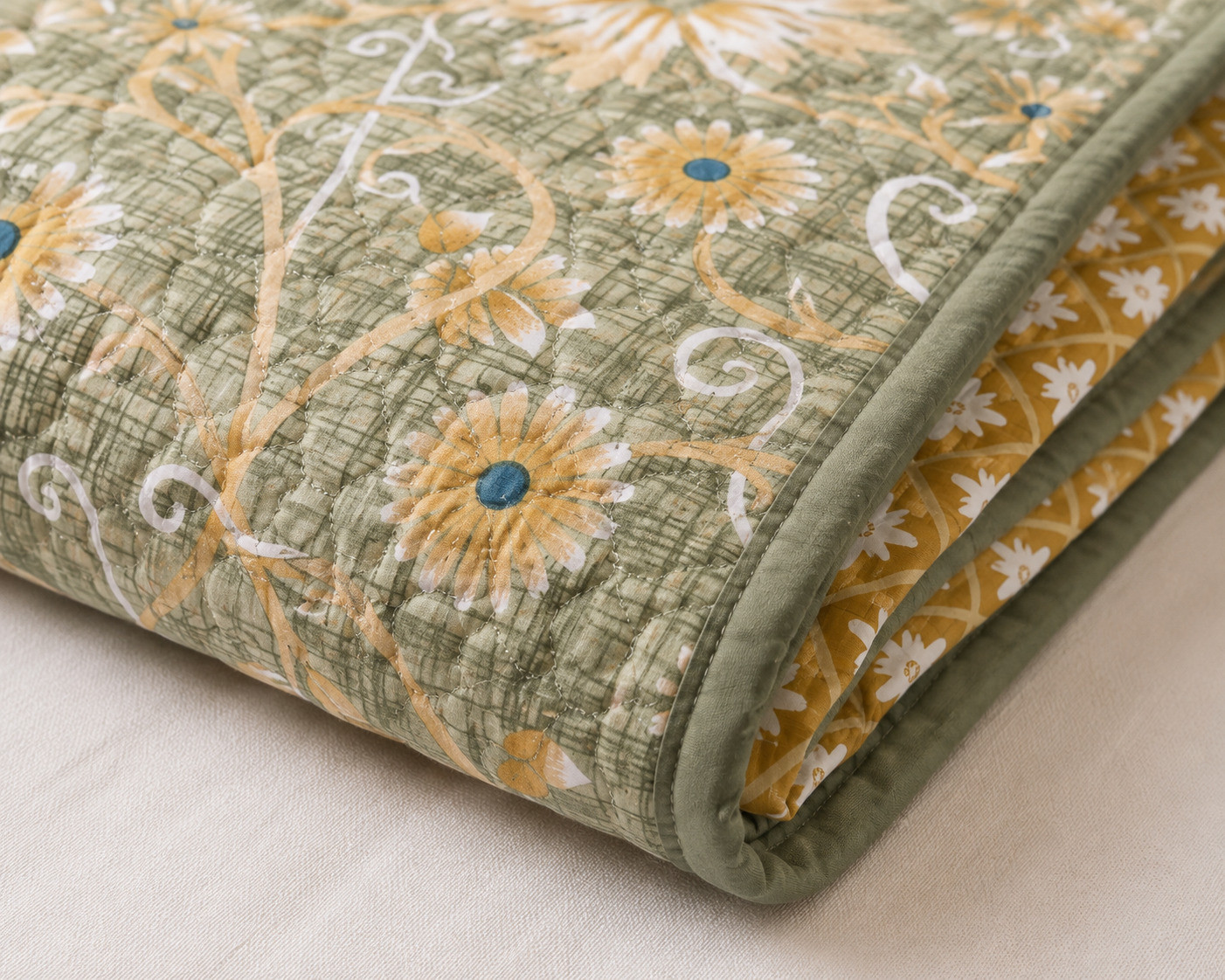 Close-up of folded sage green daisy quilted comforter showing floral vine print and mustard trellis reverse side