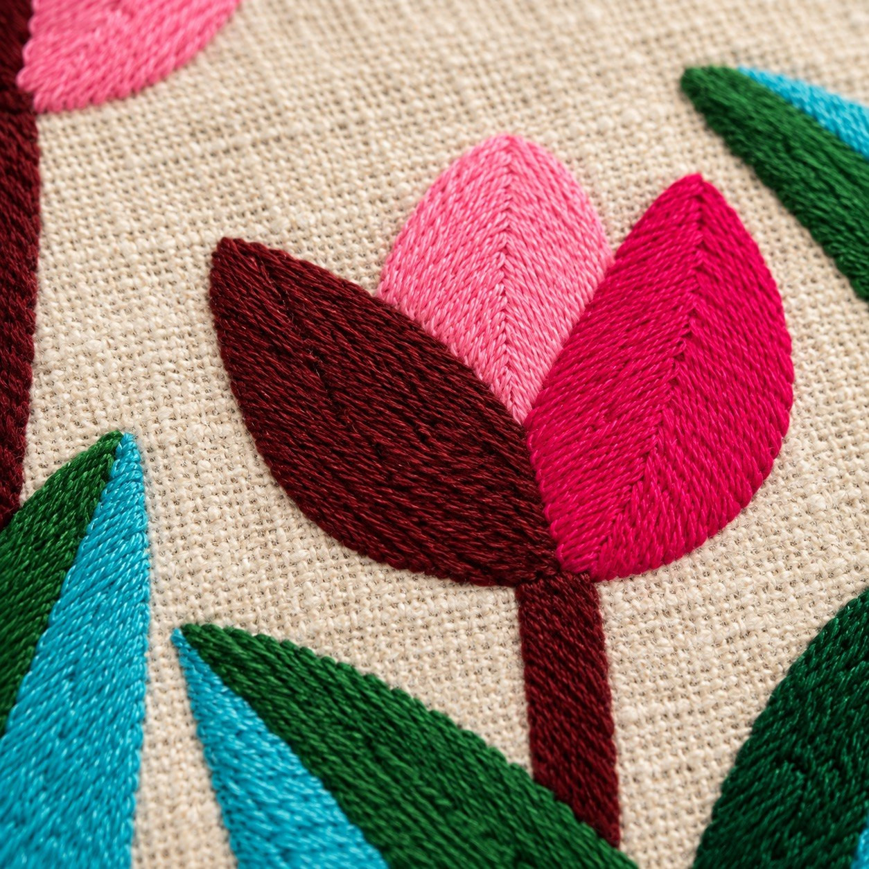Close-up of hand embroidered maroon and pink tulip with teal and green blade leaves