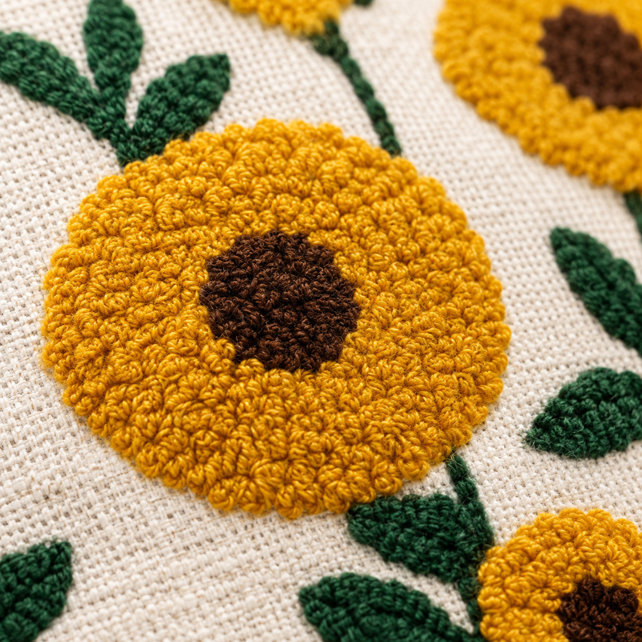 Close-up of hand embroidered mustard sunflower with dark brown center and green leaves