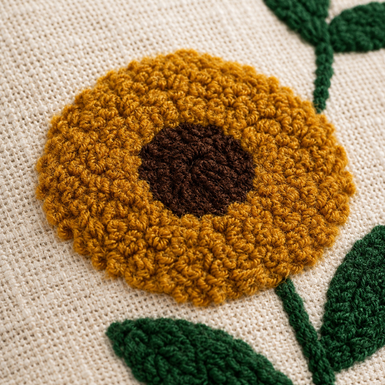 Close-up of hand embroidered mustard yellow sunflower with dark brown center and green leaf