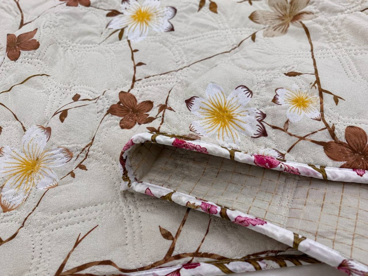 Close-up of ivory cotton quilted comforter with blossom branch print showing wave-stitch quilting and floral piped edge