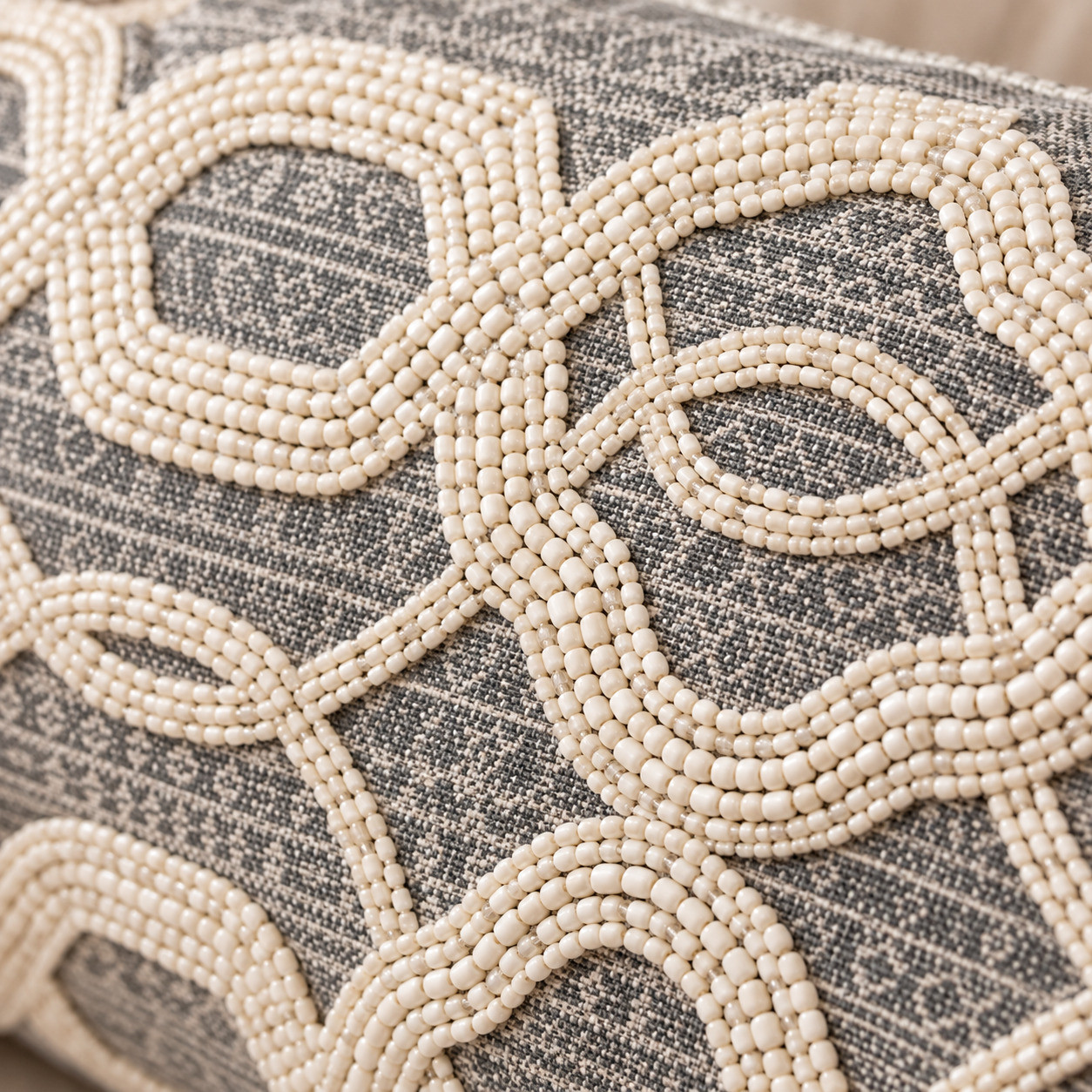 Close-up of ivory seed bead trellis embroidery on gray cushion fabric