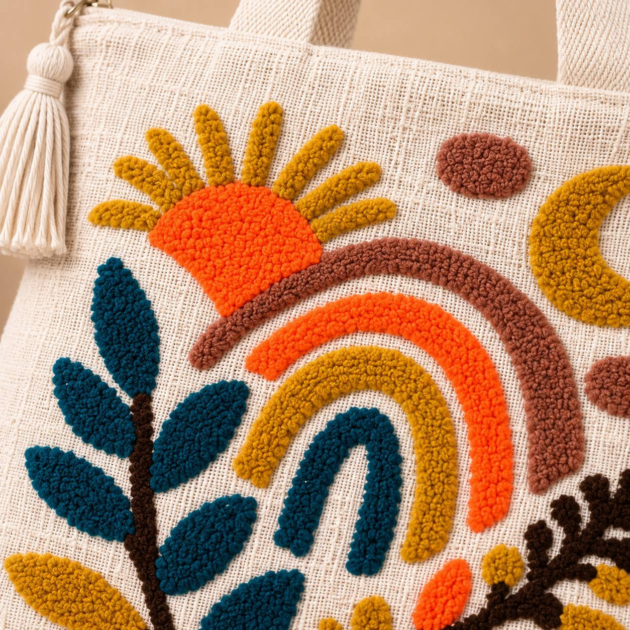 Close-up of punch-needle sun rainbow and leaf embroidery detail with tassel zipper pull