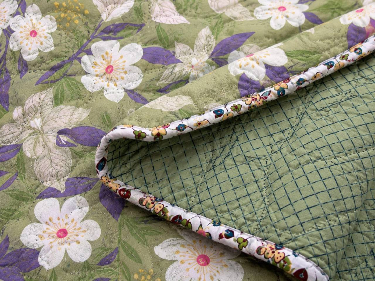 Close-up of sage green floral cotton quilted comforter showing wave-stitch quilting and floral piped edge
