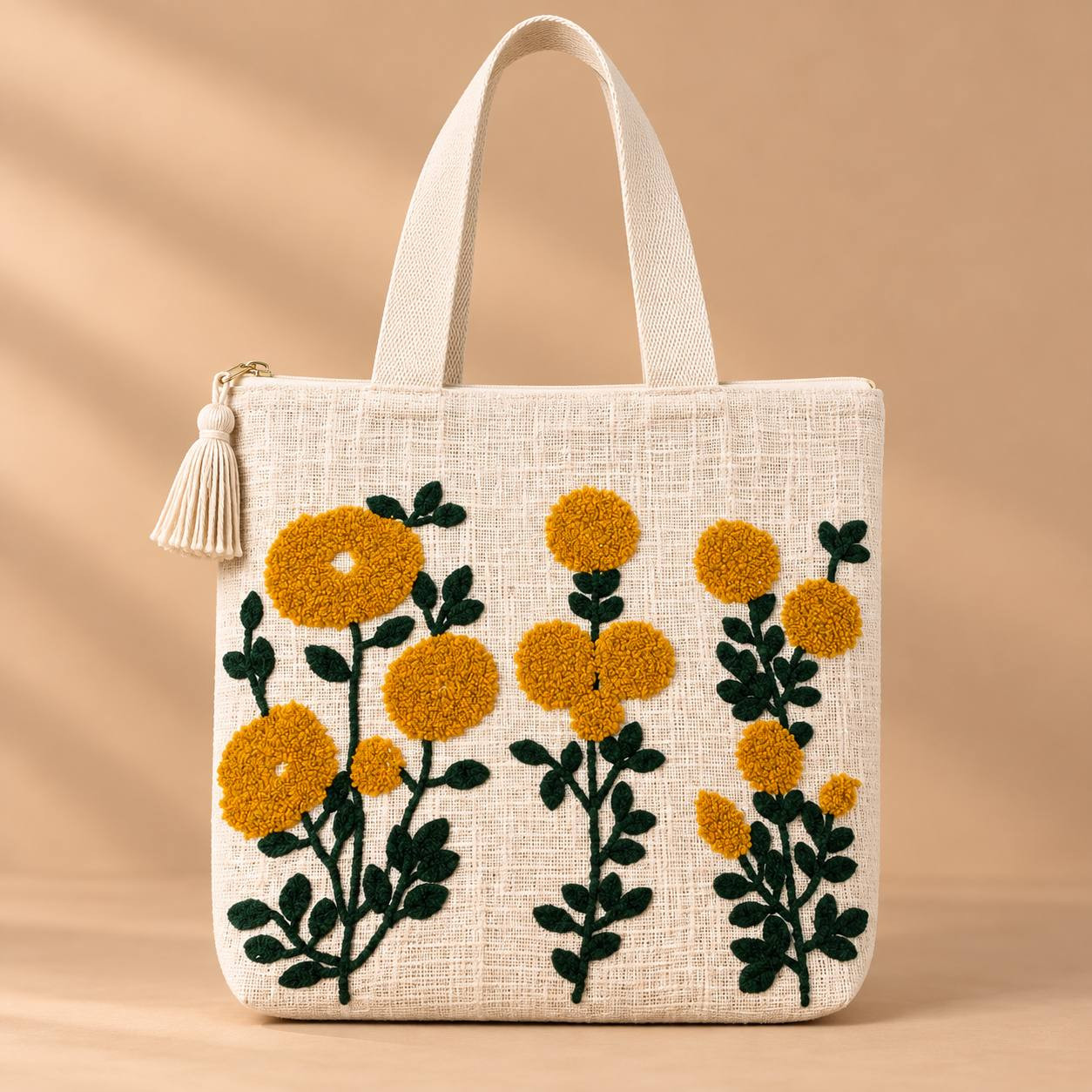 Marigold embroidered cotton slub tote bag with tassel zipper pull on beige background