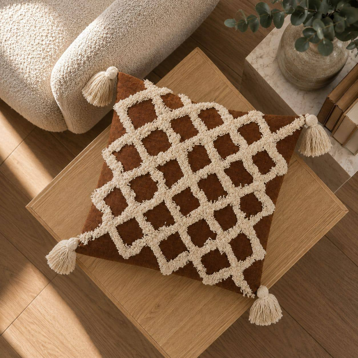 Top view of rust brown tufted diamond pattern cushion cover with cream tassels on wooden coffee table