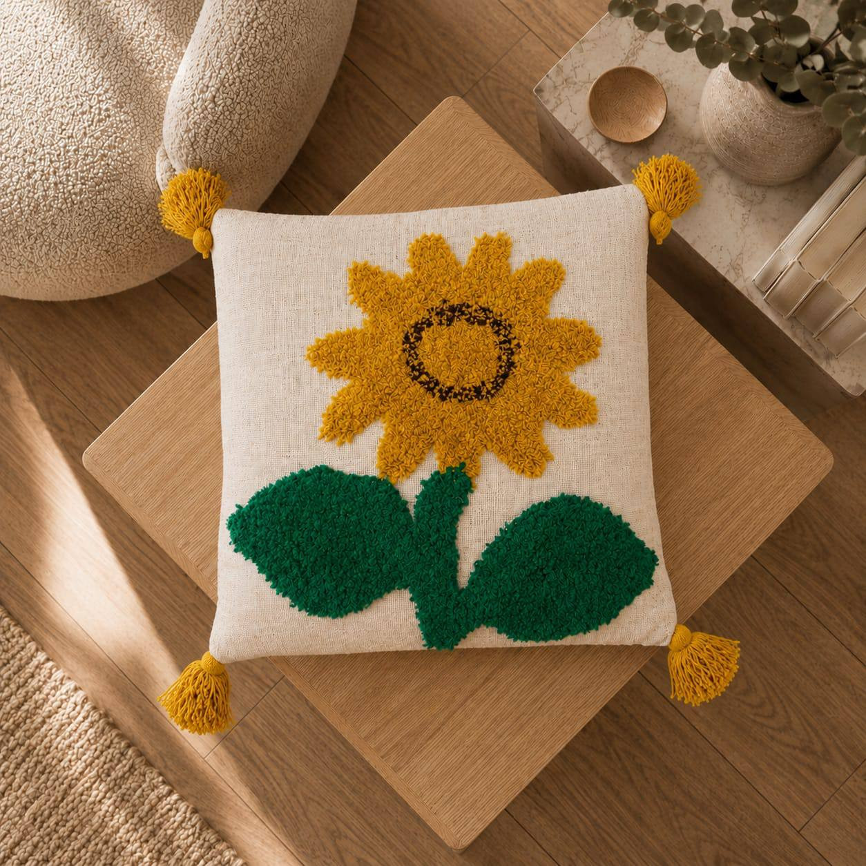 Top view of cream sunflower tufted cushion cover with yellow tassels on wooden coffee table